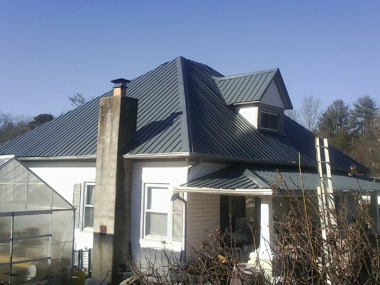 Dark blue standing seam metal roof on a white farmhouse with dormer — Slate & Tile Roof Repair by Roofing Brothers in Bertha