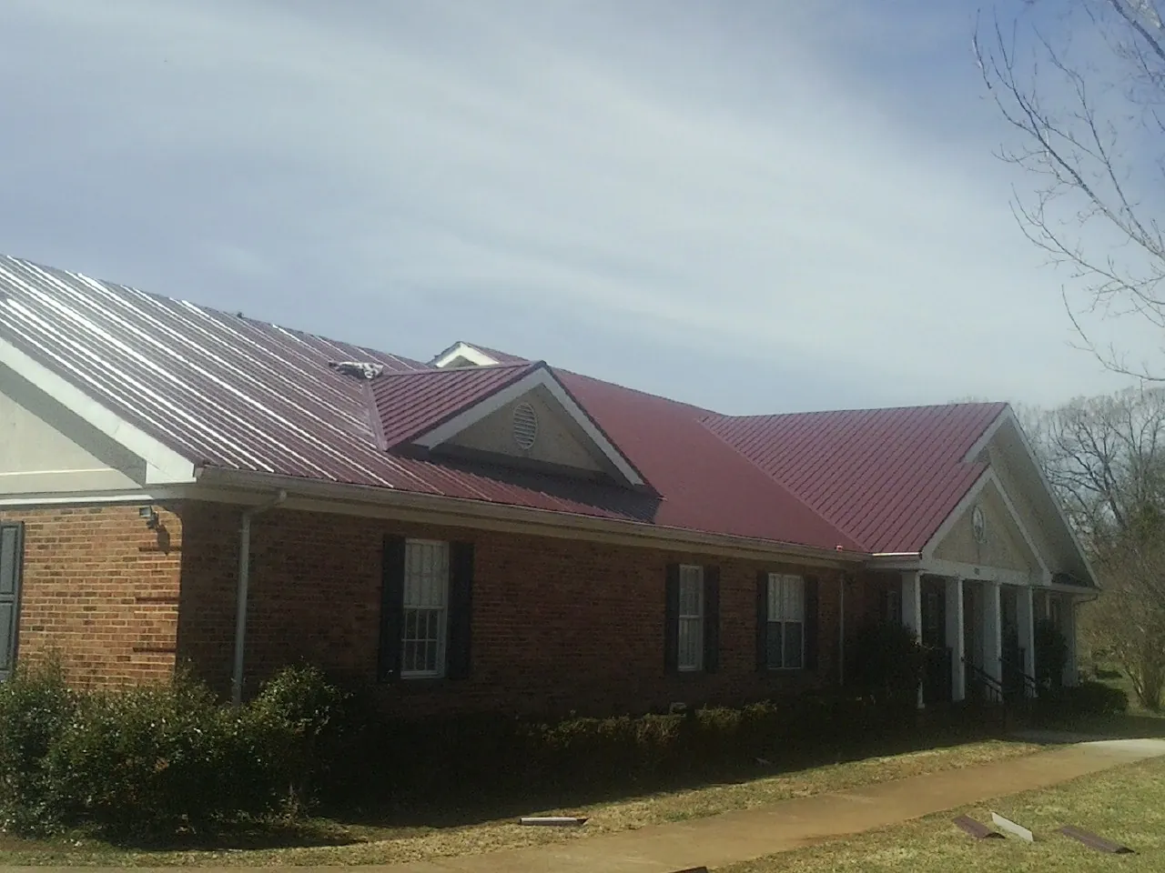 Red metal roof with gabled entries on a long brick building, from a Hail Damage Roof Repair job in Bertha