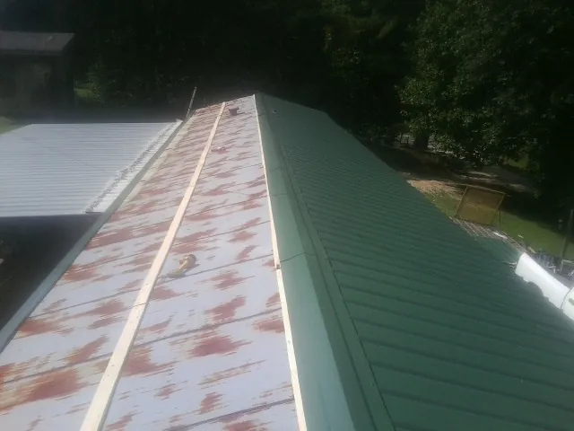 Old rusted panels beside newly installed green metal roofing — Wind Damage Roof Repair by Roofing Brothers in Bertha