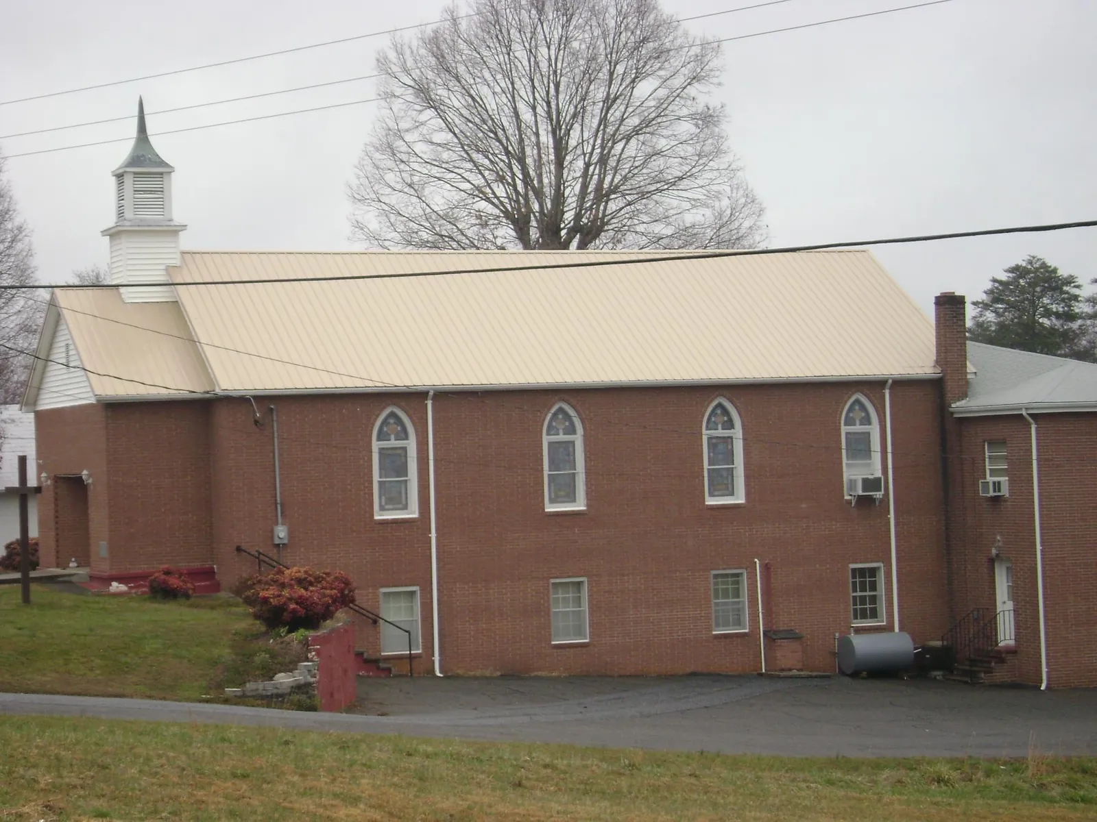 New tan metal roof on a brick church with a white steeple in Bertha