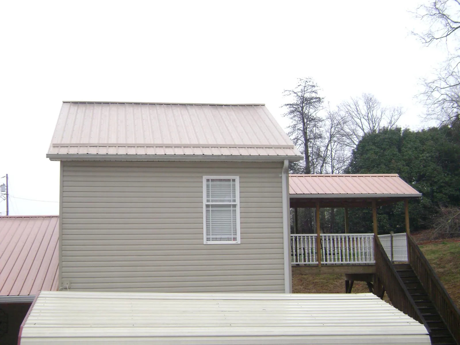Tan metal roofs on a two story addition and attached porch, from a Roof Replacement job in Bertha